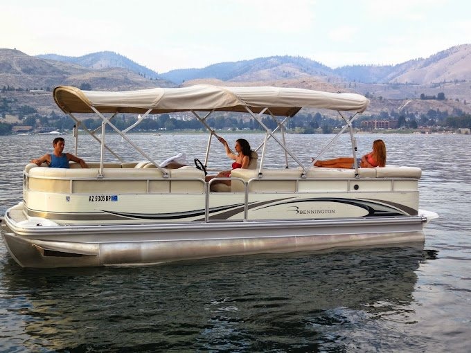 Three people relaxing on a pontoon boat with canopy on Lake Chelan surrounded by mountains